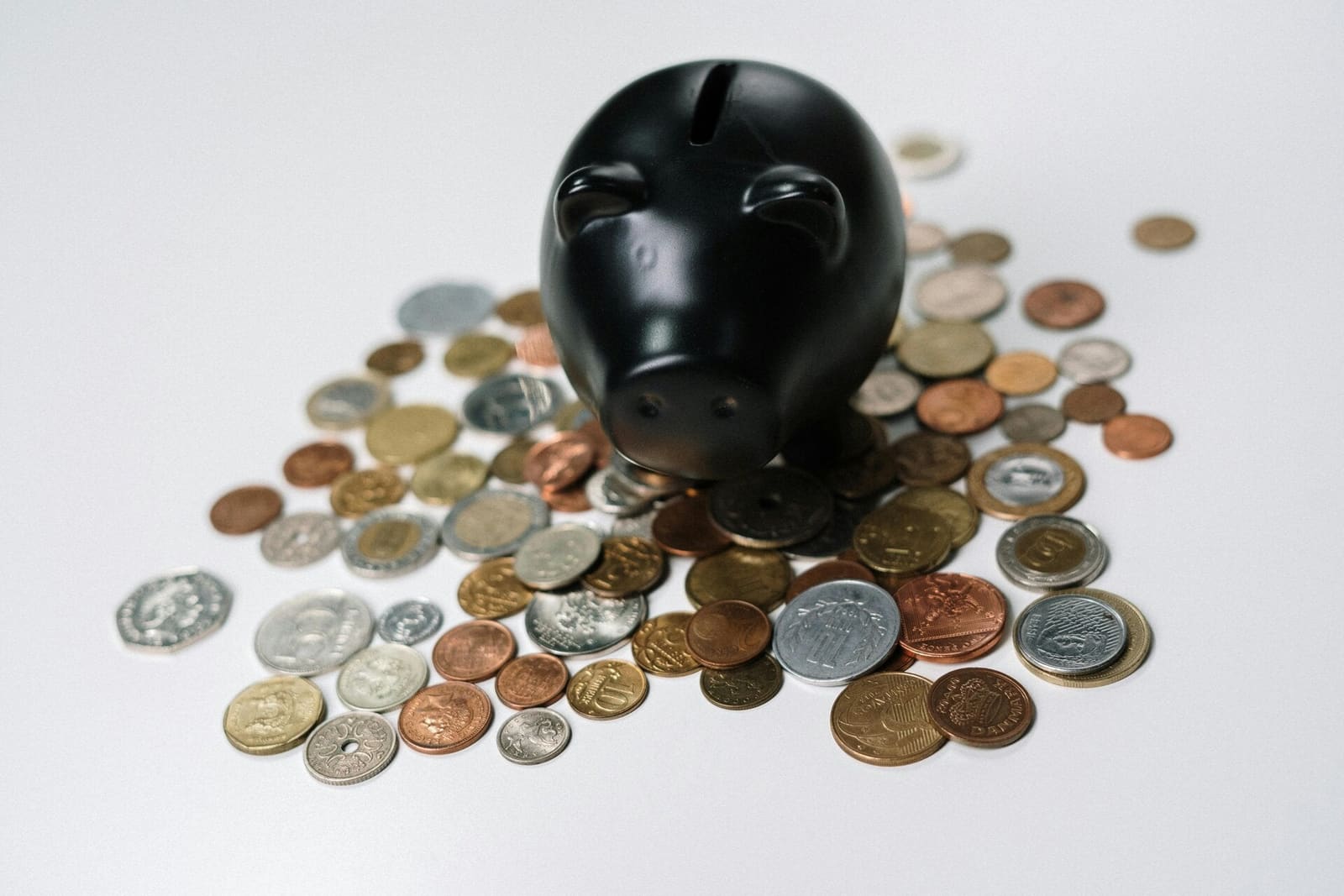 Hucha negra rodeada de monedas de distintos países sobre una mesa blanca